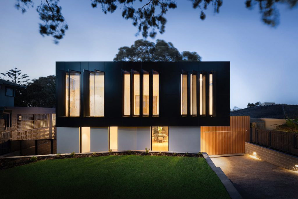 Modern Black Facade Home at Dusk – ideal jewelry and loan Contemporary two-story house with a sleek black upper facade, tall vertical windows, wood paneling, and illuminated interiors – ideal jewelry and loan