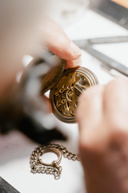 Close-up of a skilled watchmaker repairing the intricate inner mechanism of a vintage pocket watch with tools on a white surface – ideal jewelry and loan