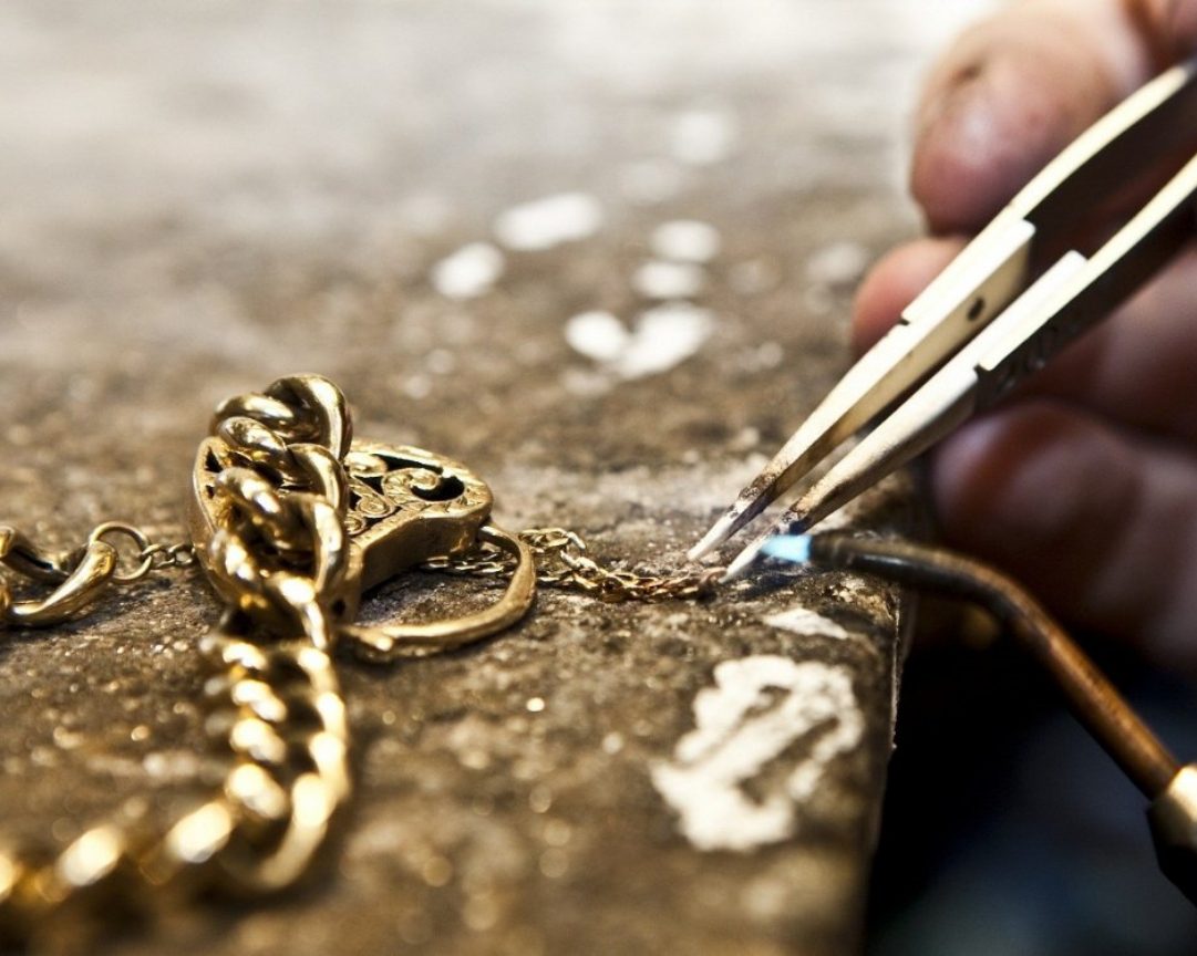 Close-up of a jeweler using pliers and a torch to repair a gold chain on a workbench – ideal jewelry and loan