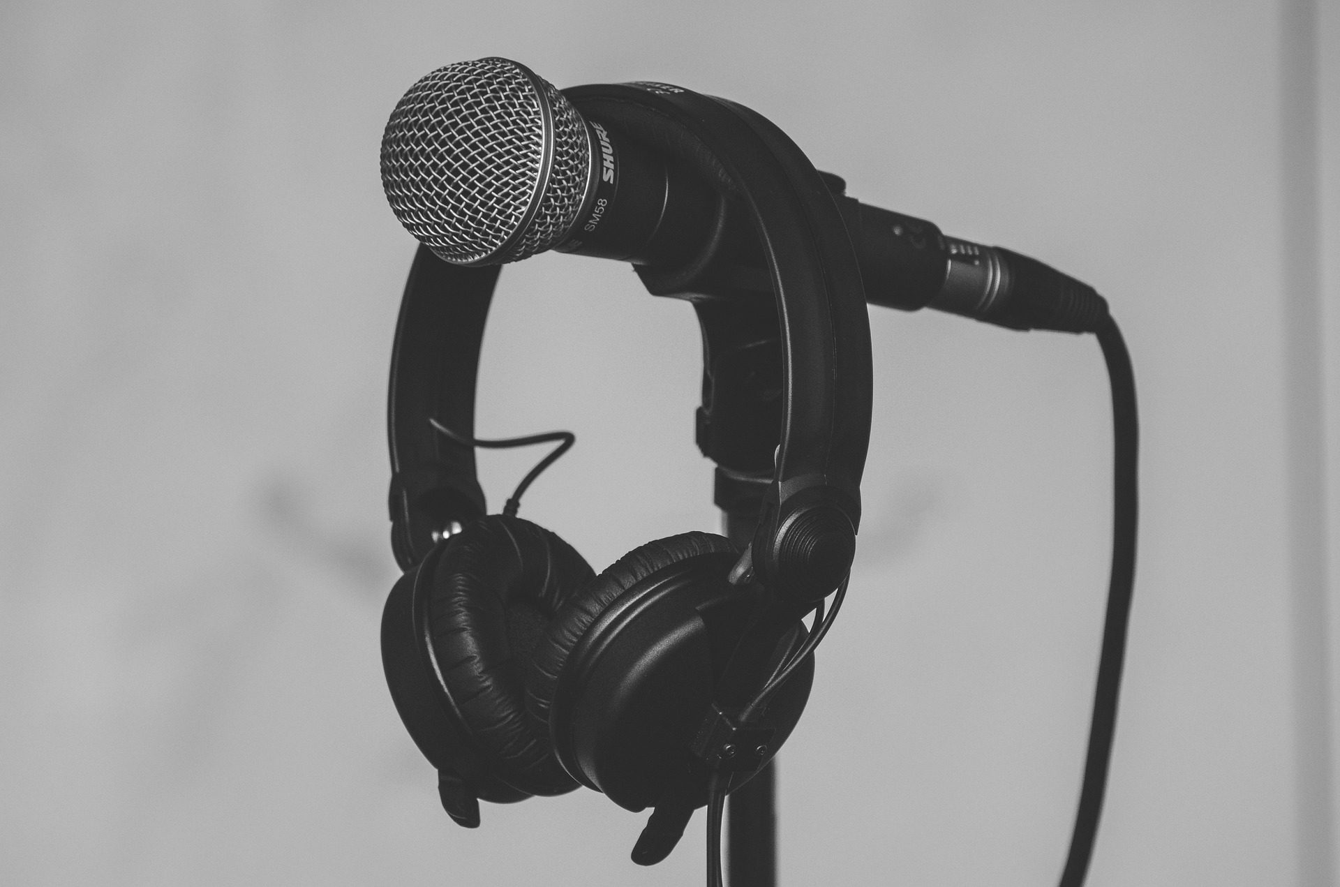 Black Shure microphone with a pair of studio headphones hanging on a mic stand in a monochrome setup.