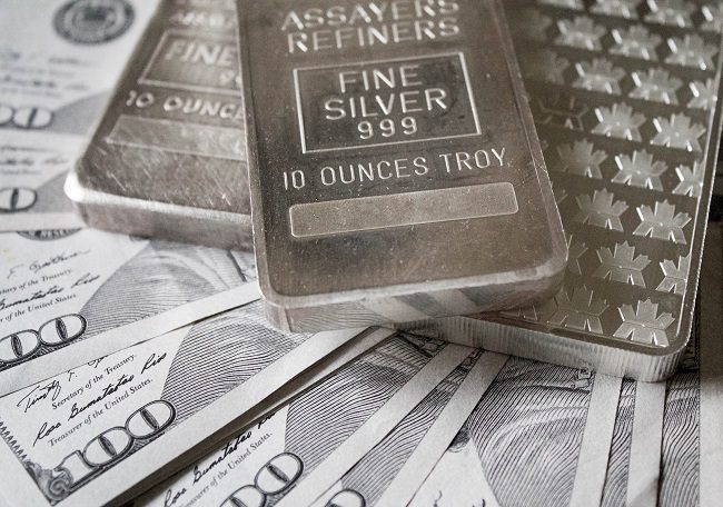Silver bullion bars marked "FINE SILVER 999, 10 OUNCES TROY" stacked on US hundred dollar bills