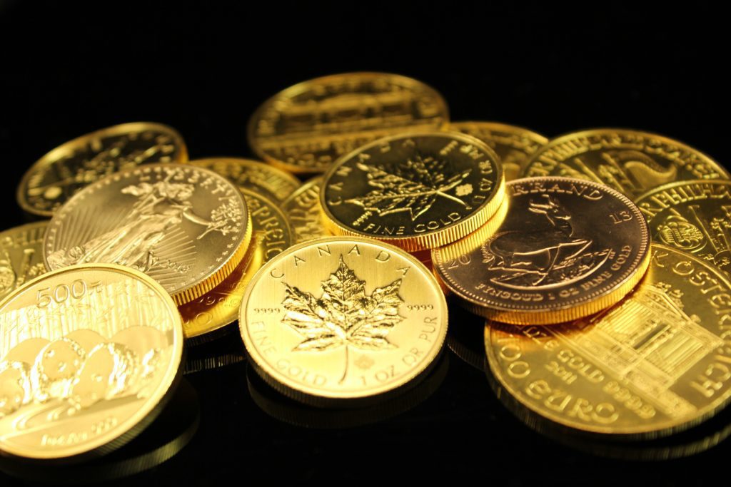 Assorted international gold coins including Canadian Maple Leaf, Krugerrand, and American Eagle on a black background