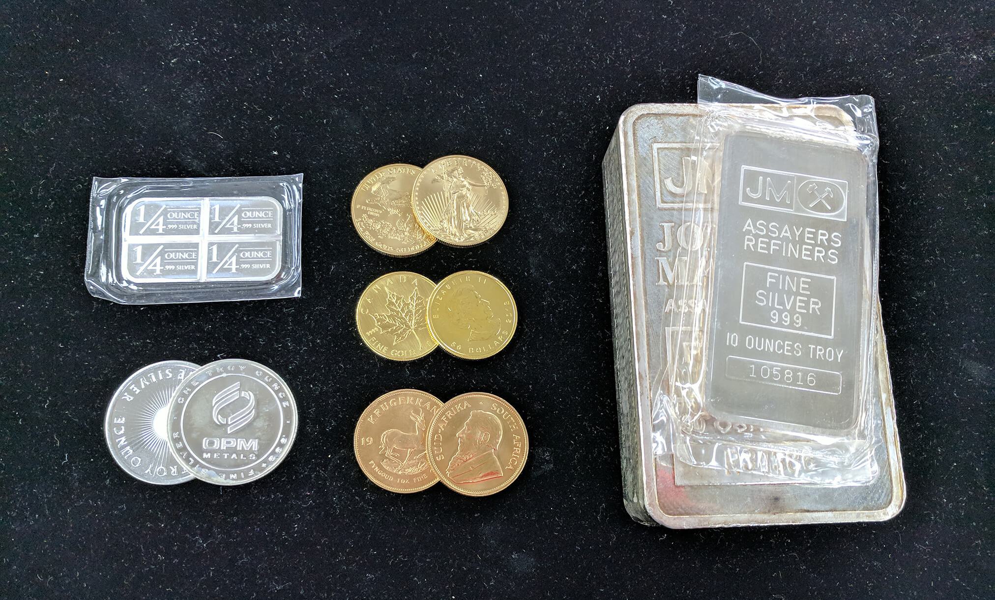 Assorted gold and silver coins and bars on a black background, including 10 oz silver bars and 1/4 oz silver pieces