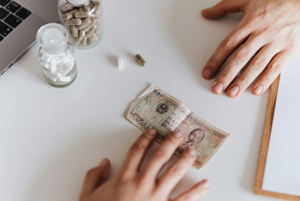 Hands exchanging currency note near supplement jars on white table.