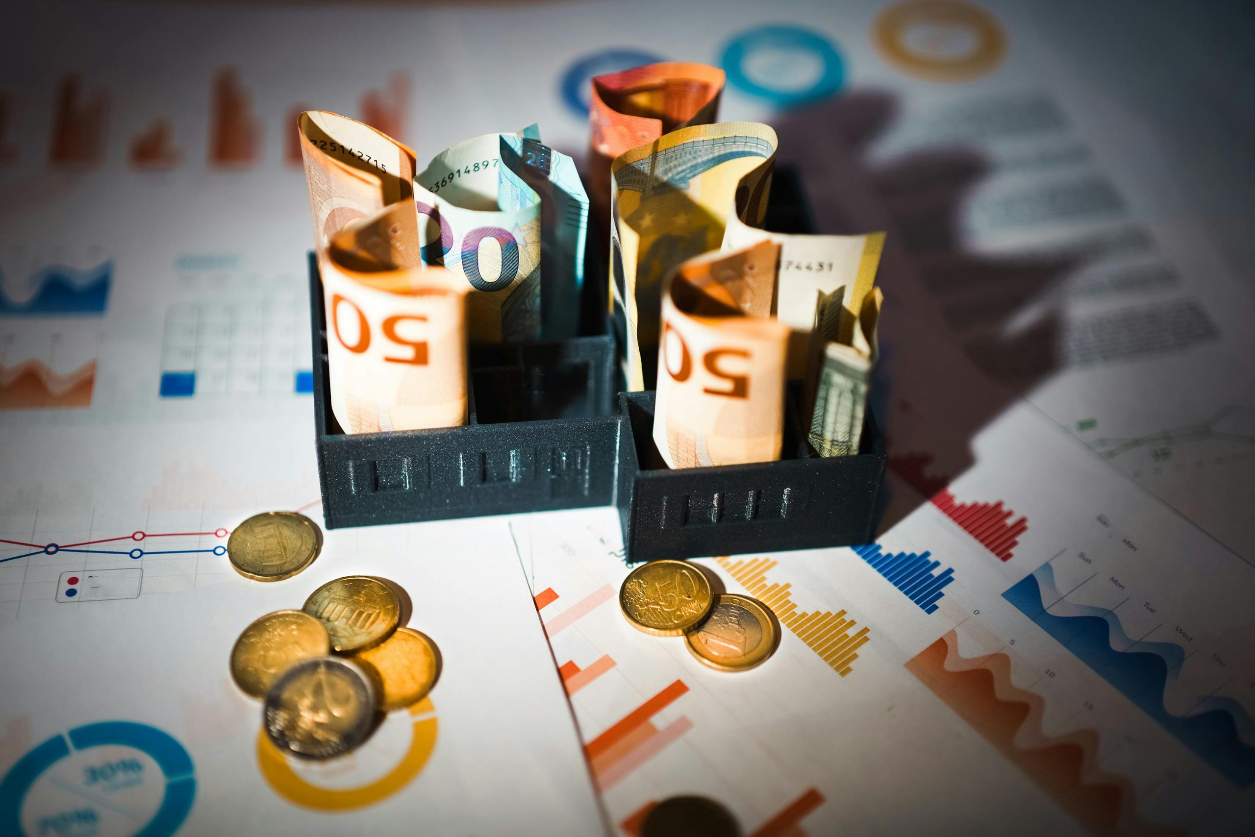 Rolled euro banknotes and coins placed on colorful financial charts