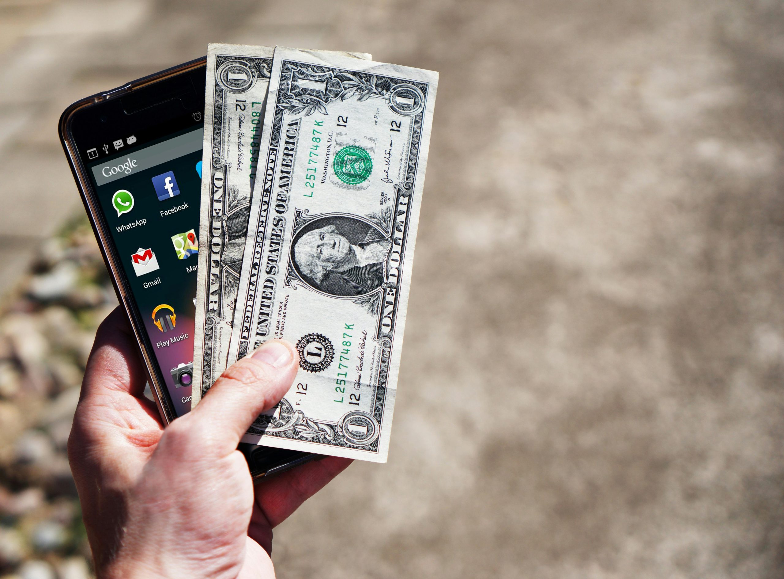 Hand holding a smartphone and a couple of dollar bills, symbolizing fast cash from a pawn shop loan