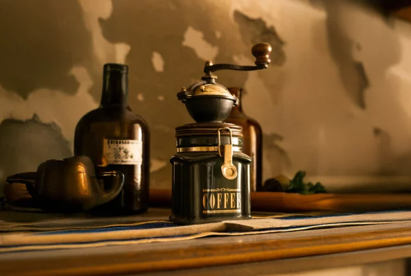 Antique manual coffee grinder with glass jar and vintage bottles on a rustic shelf