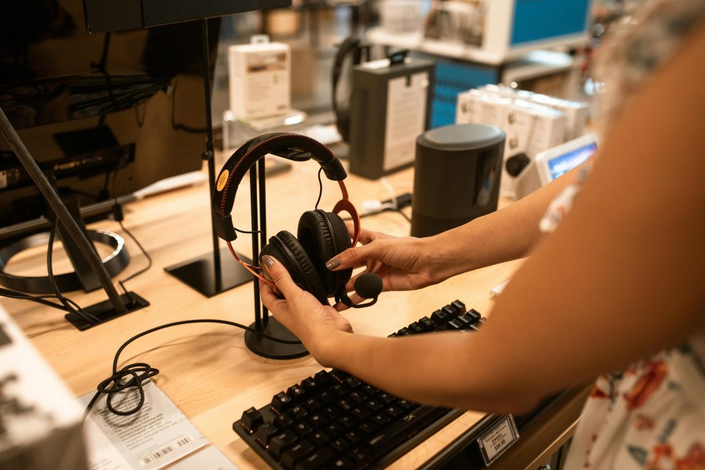 Person inspecting high-end headphones at an electronics display with keyboard and tech gadgets