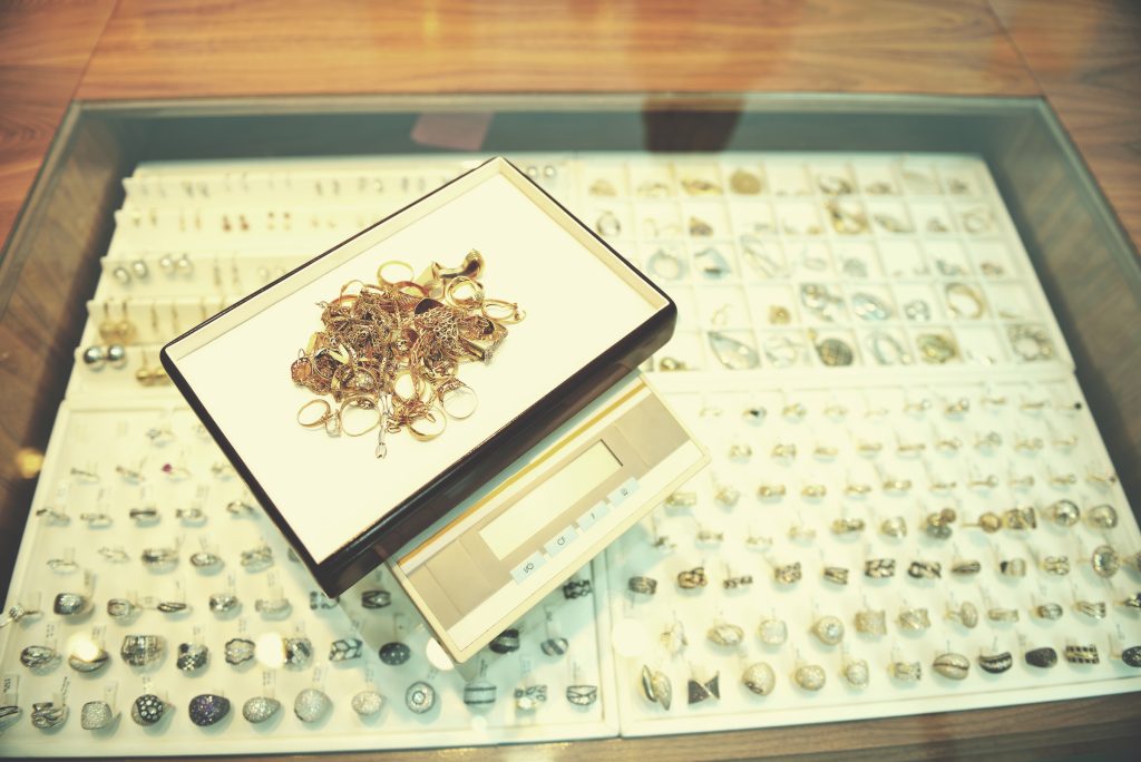 Gold jewelry on a digital scale inside a pawn or jewelry store with various rings and accessories on display