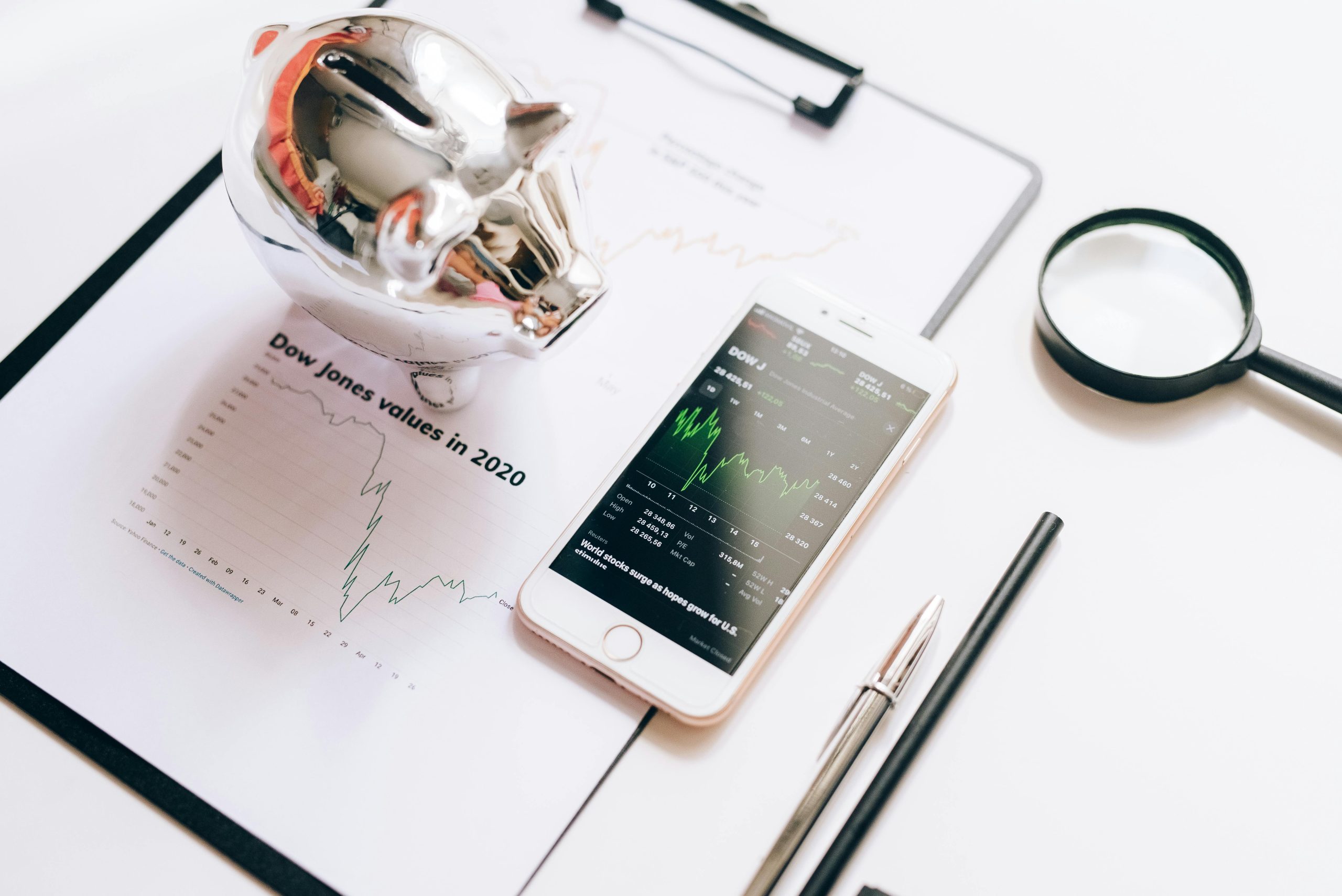 A smartphone displaying financial charts on top of documents and a piggy bank, illustrating pawn loan interest rates