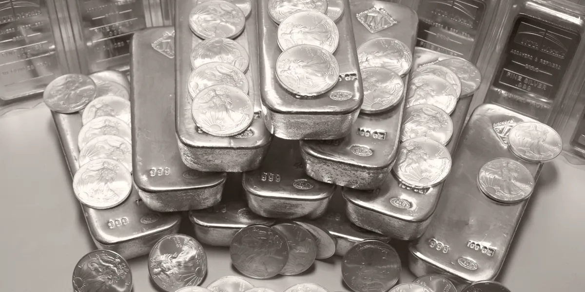 Silver bars and gold bullion stacked with dollar bills on a wooden table