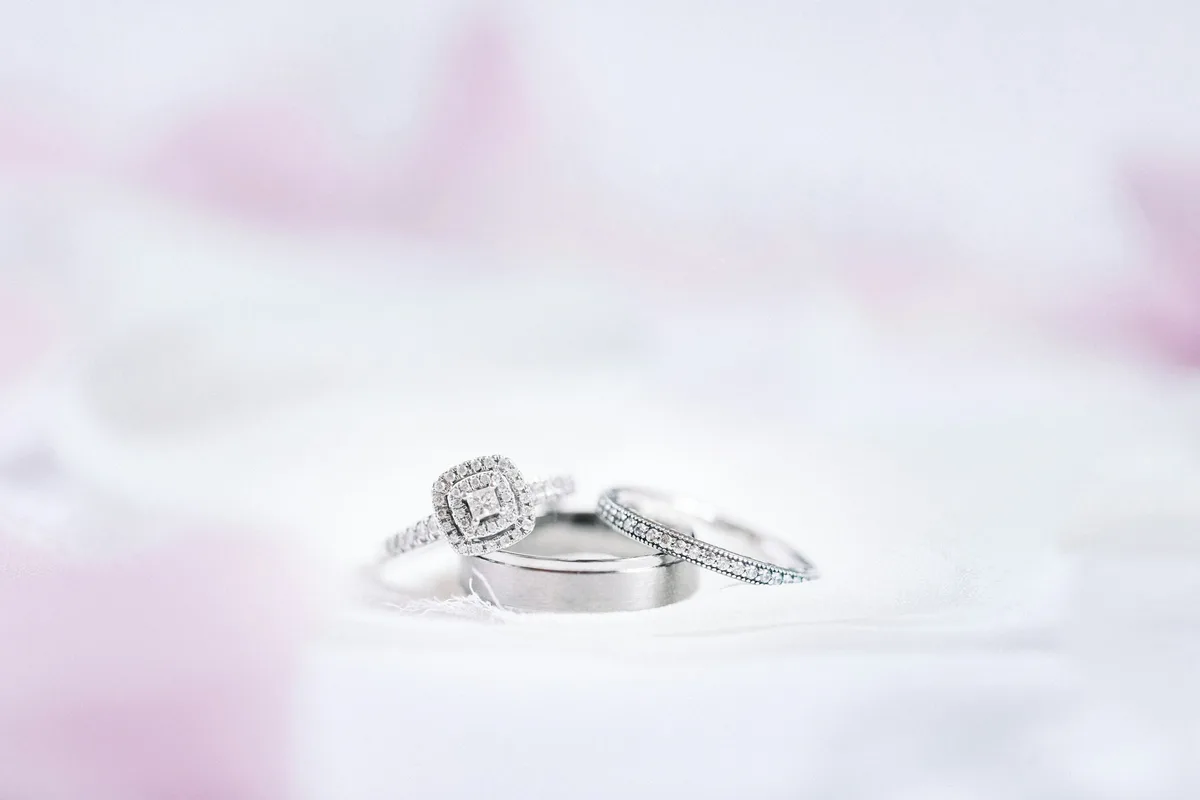 An engagement ring and two wedding bands in white metal resting on soft white fabric
