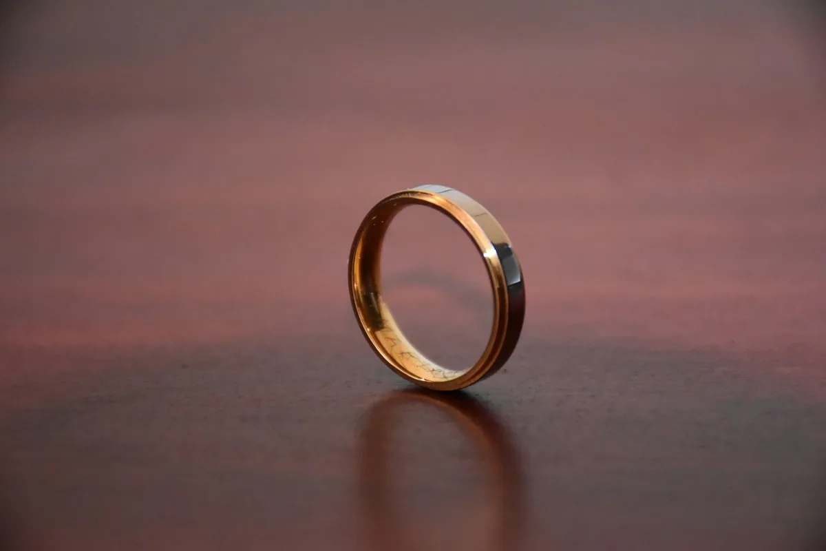 A gold ring band standing on a polished wooden table