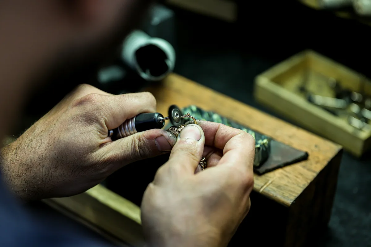 A jeweler's hands working on a ring with a small rotary tool at a wooden bench